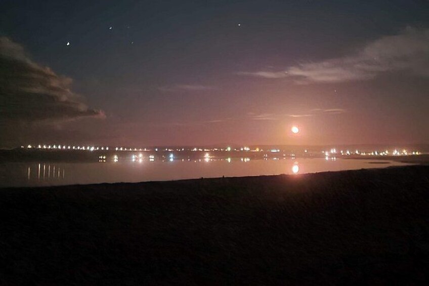 A nighttime coastal scene with a calm sea, a distant city skyline, and a visible moon. 5