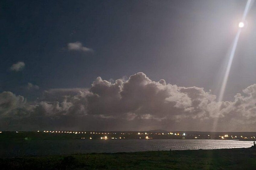 A night sky with clouds, a bright moon, and distant city lights. 3