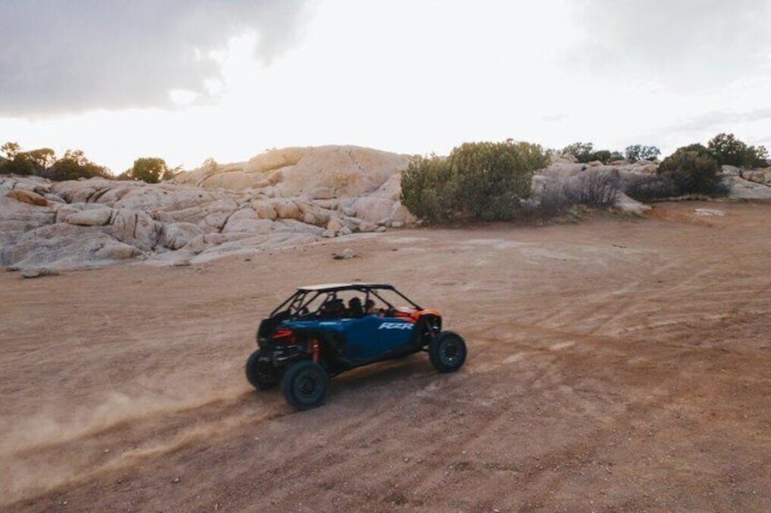 A blue off-road vehicle on a dirt road with rocky terrain and sparse vegetation. 4