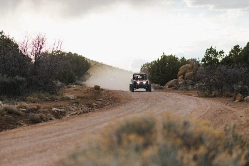 A vehicle on a dirt road surrounded by sparse vegetation and rocks. 1