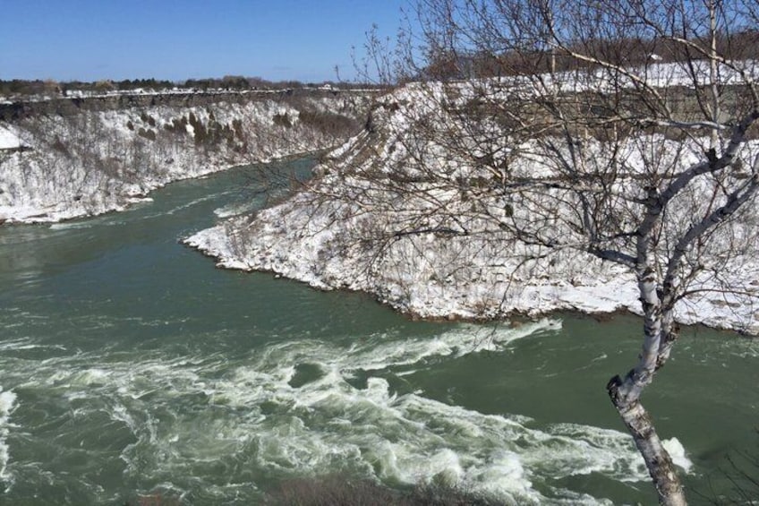 A river flowing through a snowy landscape with bare trees and rocky cliffs. 5