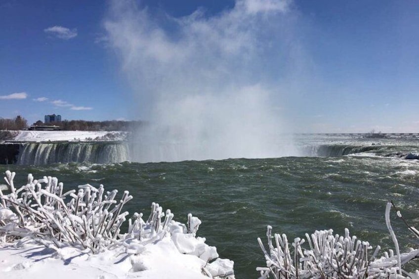 A frozen waterfall with ice formations in the foreground and a cityscape in the background. 1