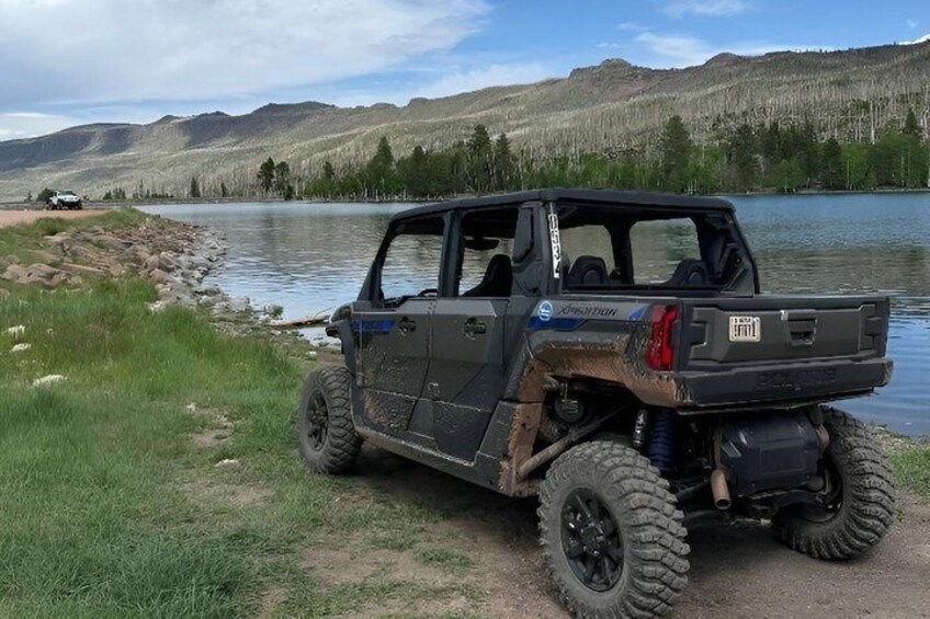 A black off-road vehicle parked by a lake with mountains in the background. 1