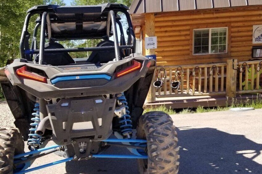 A Polaris RZR ATV parked in front of a wooden cabin with a porch. 5