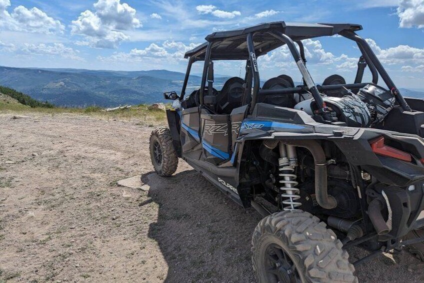 A Polaris RZR off-road vehicle parked on a dirt path with a mountainous landscape in the background. 5