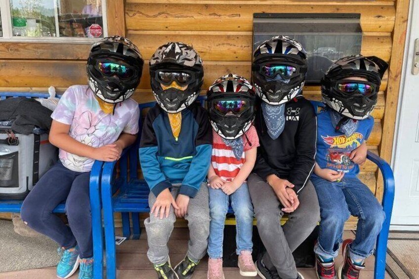 Four children sitting on a bench wearing helmets. 3