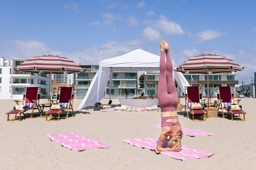 A person doing a handstand on a beach with beach chairs and umbrellas in the background. 3