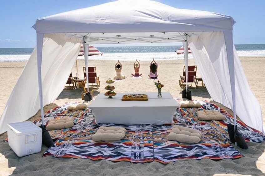 A beach tent setup with a dining table, cushions, and beach chairs. 2