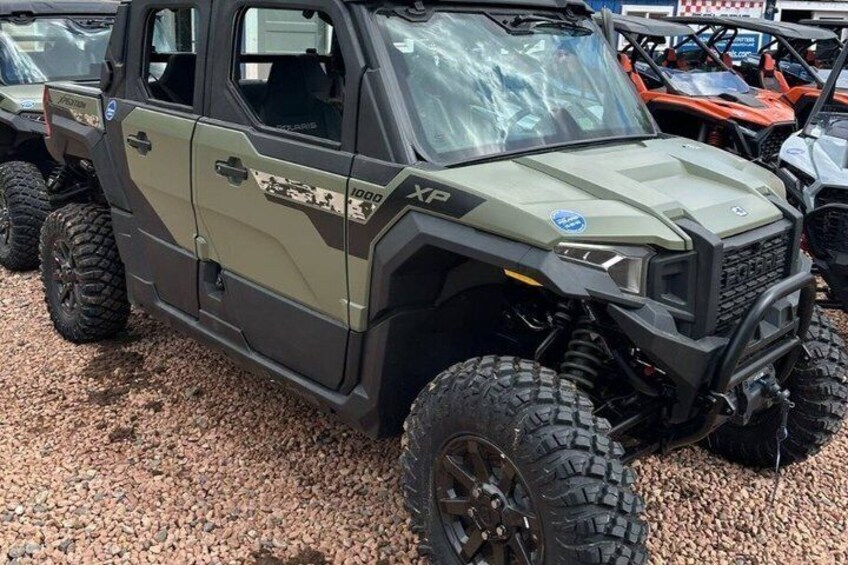 A rugged off-road vehicle with large tires and a camouflage pattern, parked on gravel. 4