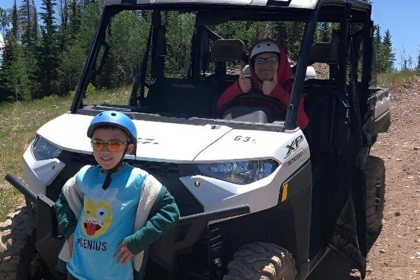 A person in a blue shirt with a cartoon character and a helmet, standing next to a white off-road vehicle with the number 63 on it. 1