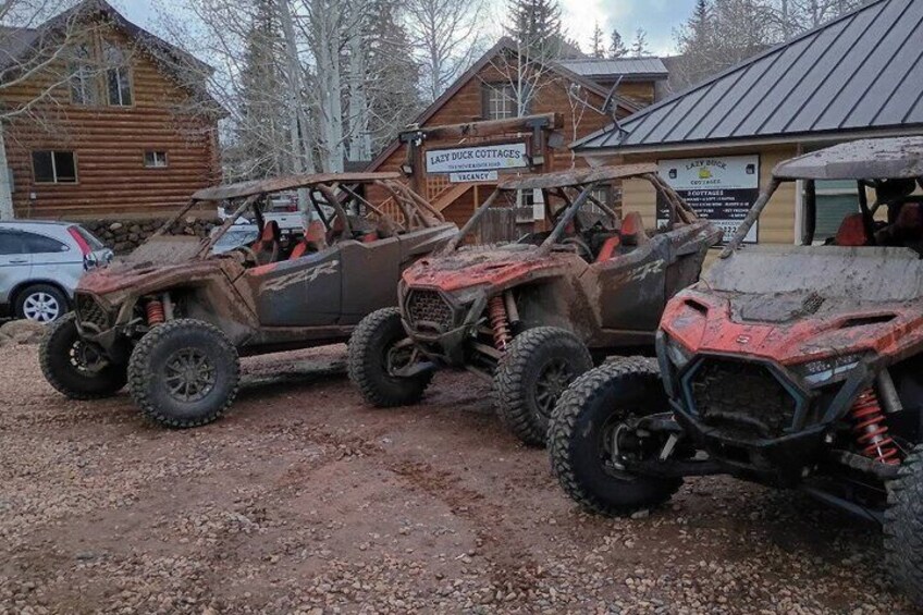 Two off-road vehicles parked in front of a rustic cabin with a sign reading 'Lazy Duck Cottages.' 2