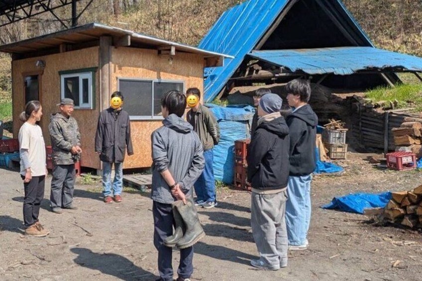 A group of people standing outdoors near a small wooden structure and a blue-roofed shed. 4