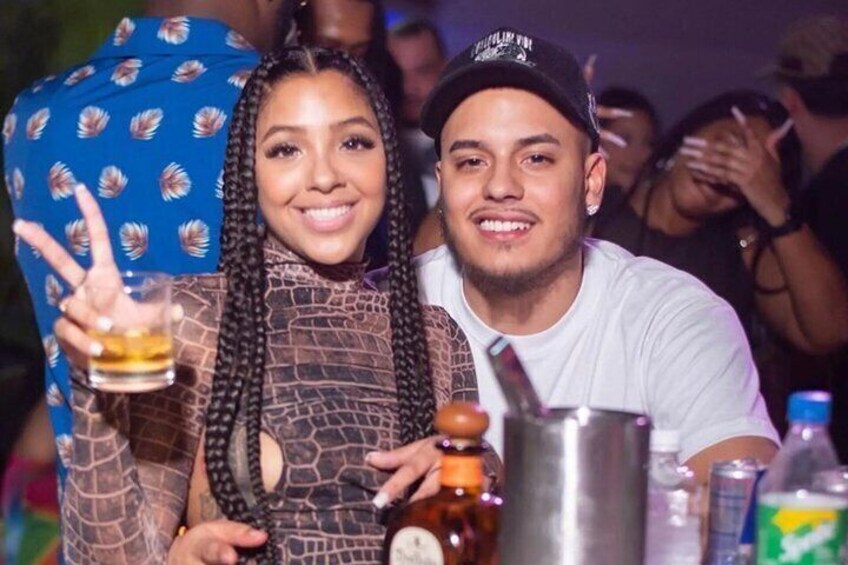 Two people at a bar with drinks and a bottle. 4