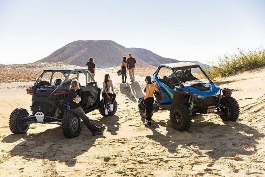 Two off-road vehicles on a sandy terrain with people around them. 5