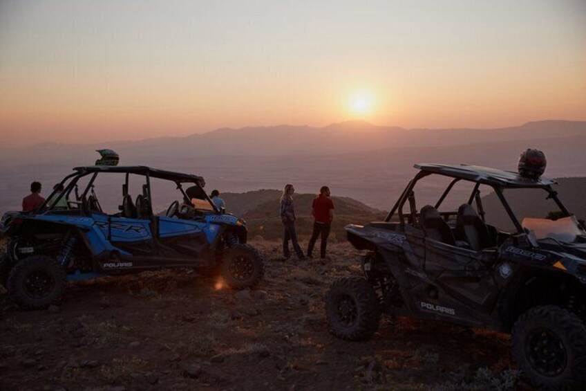 Two Polaris ATVs parked on a rocky terrain with a sunset in the background. 1
