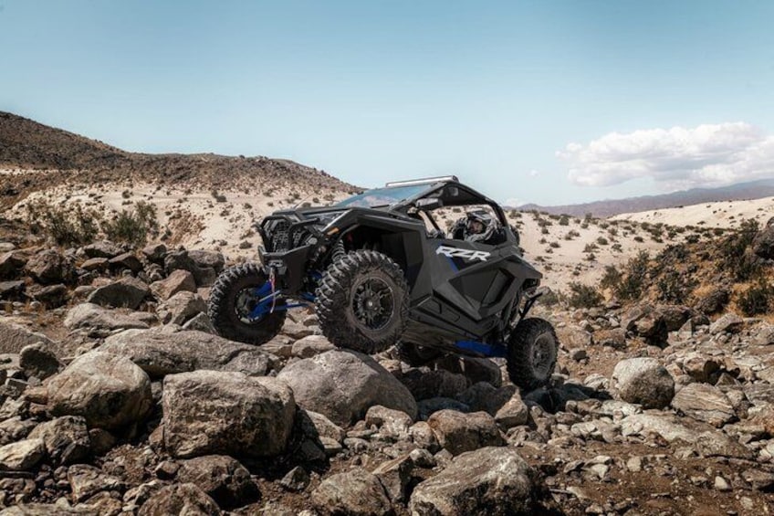 A black off-road vehicle on rocky terrain with a desert landscape in the background. 4