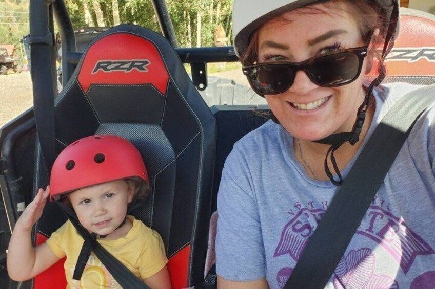 A child in a red helmet and a woman in a grey t-shirt seated in a RZR vehicle. 5