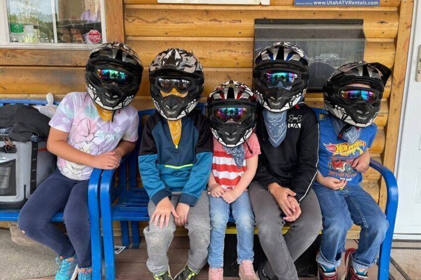 Four people sitting on a bench with helmets. 4