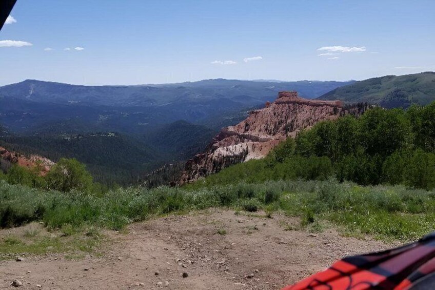 A mountainous landscape with a dirt path, green vegetation, and a red rock formation. 1