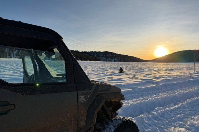 A vehicle on a snowy landscape with a person in the distance and the sun setting. 3