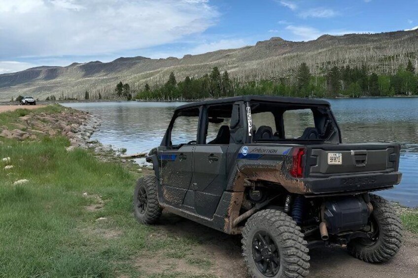 A rugged off-road vehicle parked by a lake with mountains in the background. 4