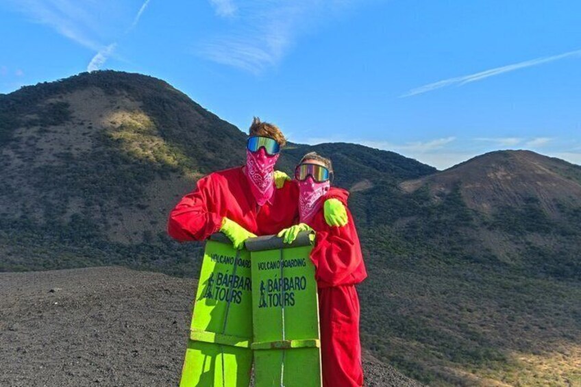 Two individuals in red protective suits standing next to a green barrel labeled 'Volcano Joya' and 'Volcano Borrego' with 'BARBARI & BARBARO' on it. 5
