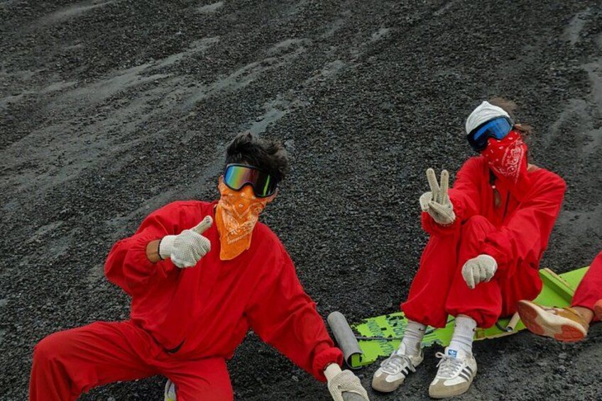 Two people in red protective suits sitting on a green sled on a rocky surface. 2