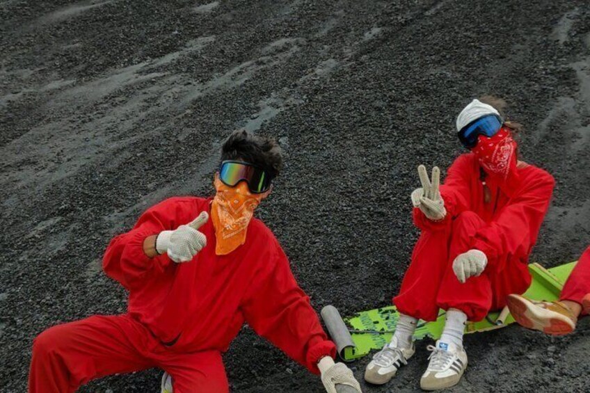 Two people in red protective suits sitting on a green sled on a rocky surface. 2