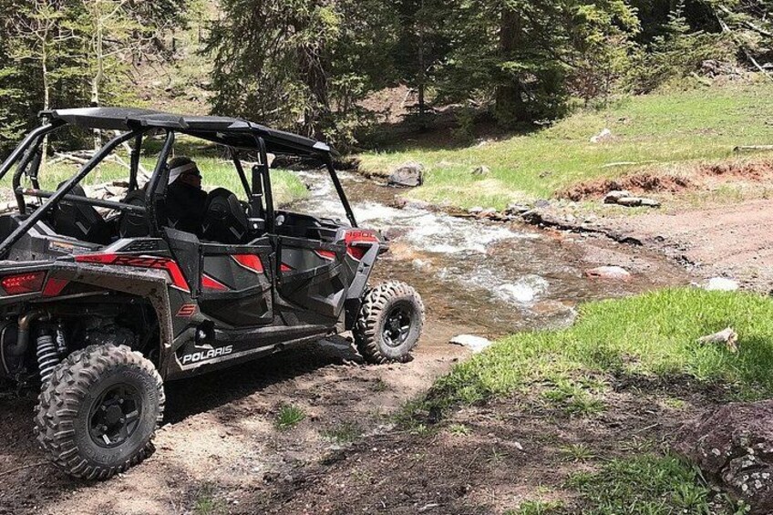A Polaris off-road vehicle on a dirt path near a stream in a wooded area. 4