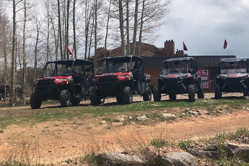 Three off-road vehicles parked on a dirt path with trees and a building in the background. 5