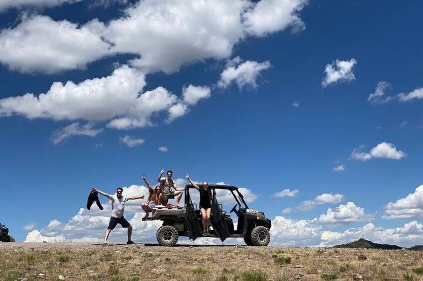 A group of people posing with a quad bike on a grassy field under a blue sky with clouds. 3
