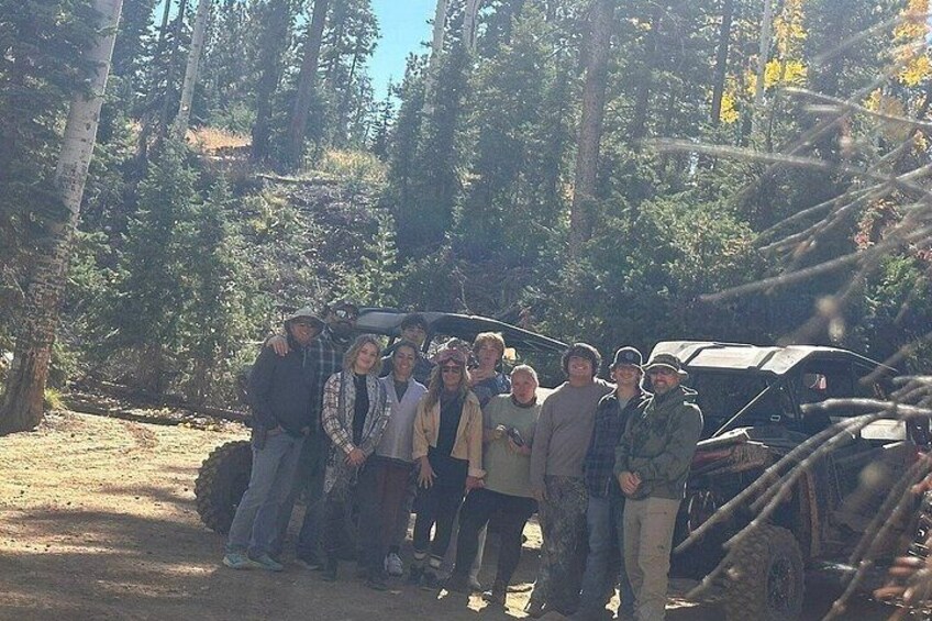 A group of people standing in a forest with a vehicle in the background. 2