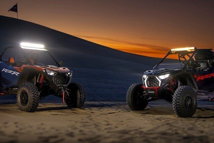 Two off-road vehicles on a sandy terrain with a sunset in the background. 3