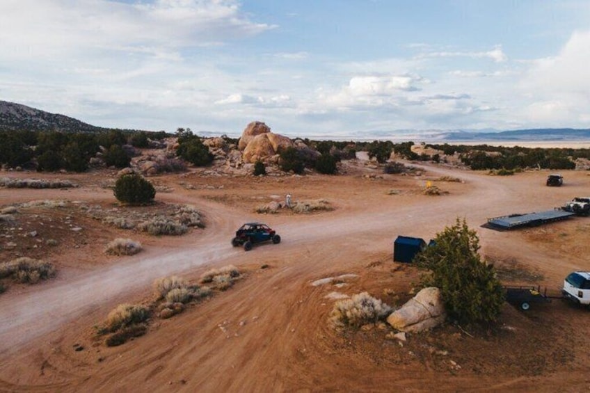 A desert landscape with a dirt road, a large rock formation, and a few vehicles. 3