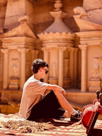 A person sitting on a patterned rug in front of a temple with columns and a dome. 5