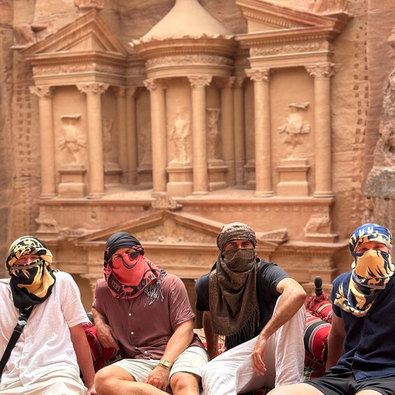 A group of people sitting in front of ancient stone architecture with columns and statues. 1