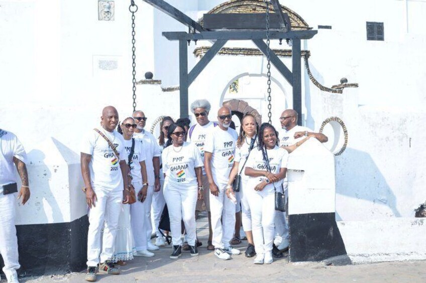 A group of people in white attire standing in front of a white wall with a black gate. 3
