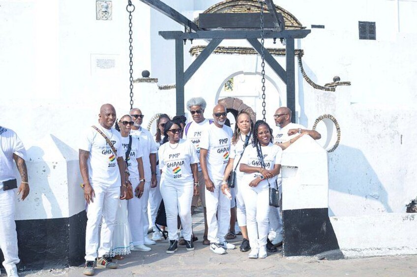 A group of people in white attire standing in front of a white wall with a black gate. 3