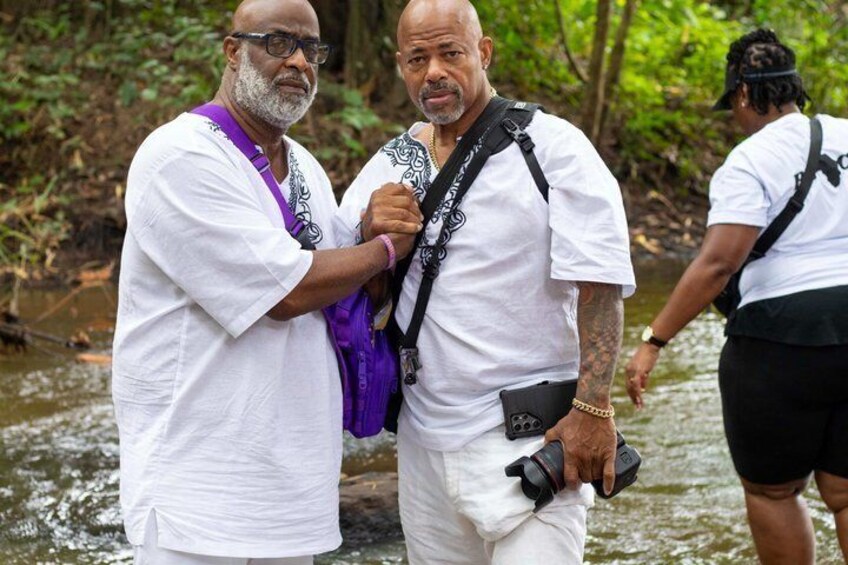 Two men in white shirts standing by a river. 1