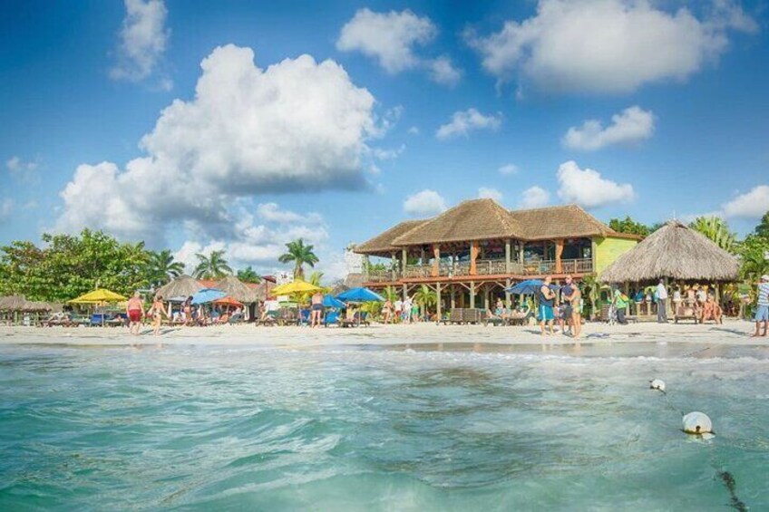 A beach with clear turquoise water, a thatched-roof building, and colorful umbrellas. 2