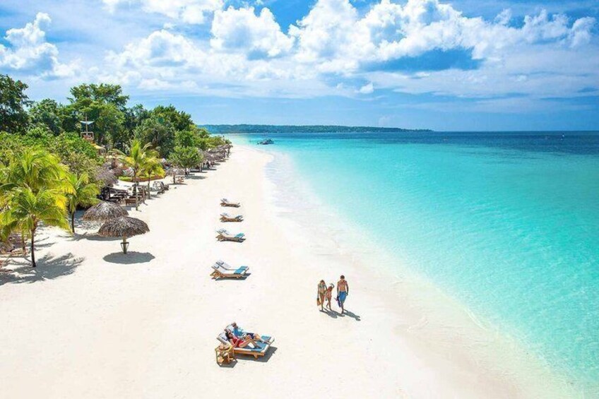 A beach with clear turquoise water, palm trees, and beach chairs. 3
