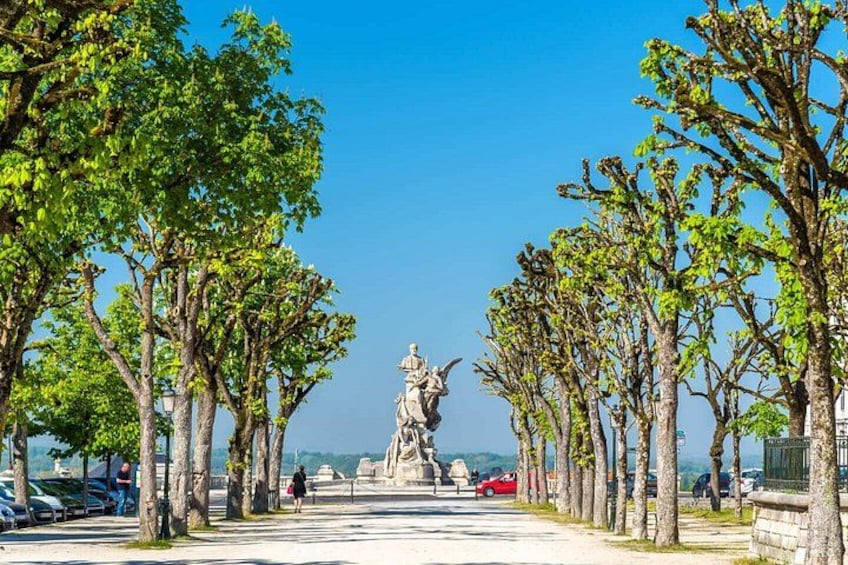 A statue in the center of a tree-lined pathway with cars parked on the side. 5