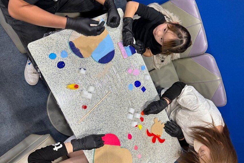 A group of people engaged in a craft activity with various colored materials on a table. 1