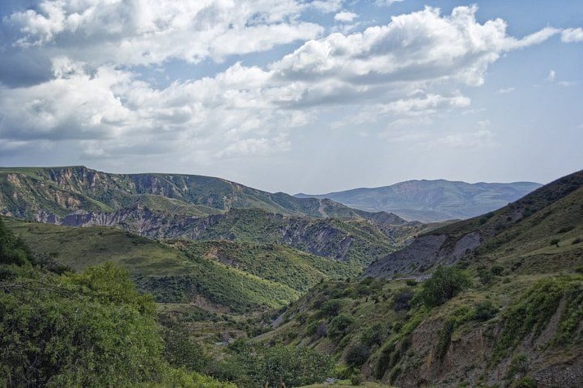 A mountainous landscape with green valleys and rocky outcrops under a partly cloudy sky. 4