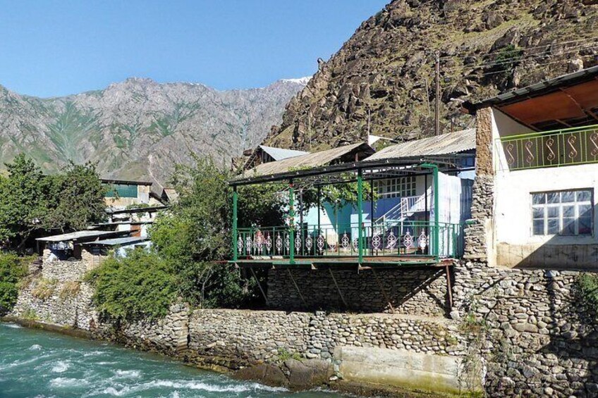 A stone bridge over a river, a building with a green balcony, and mountains in the background. 2