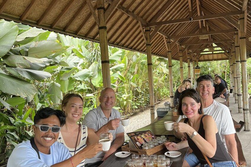 A group of people sitting at an outdoor table with food and drinks, surrounded by tropical plants. 4