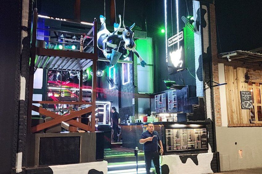 A person standing in front of a building with a neon sign and a hanging sculpture. 4