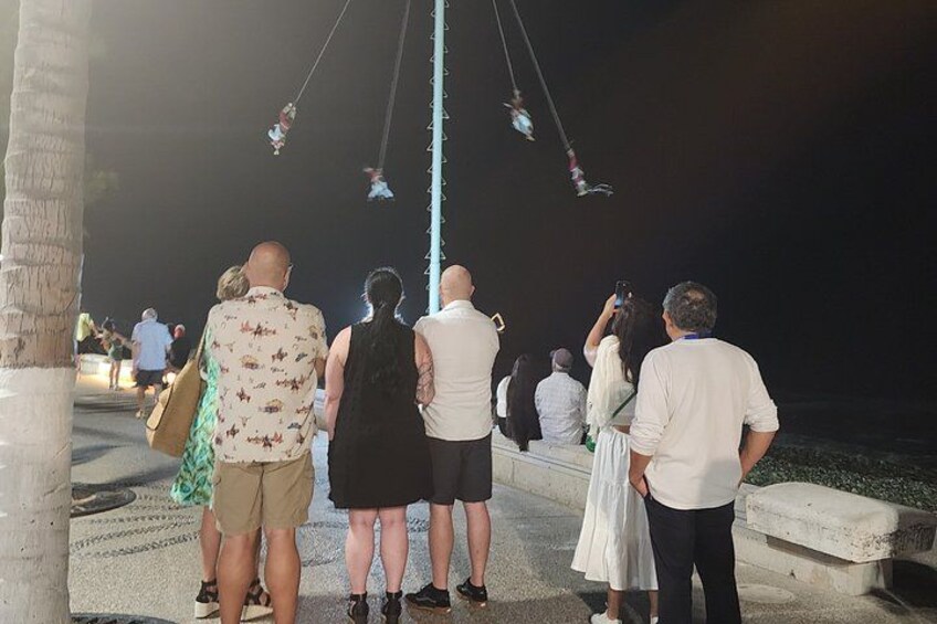 People standing on a concrete walkway, looking at a vertical pole with lights. 3