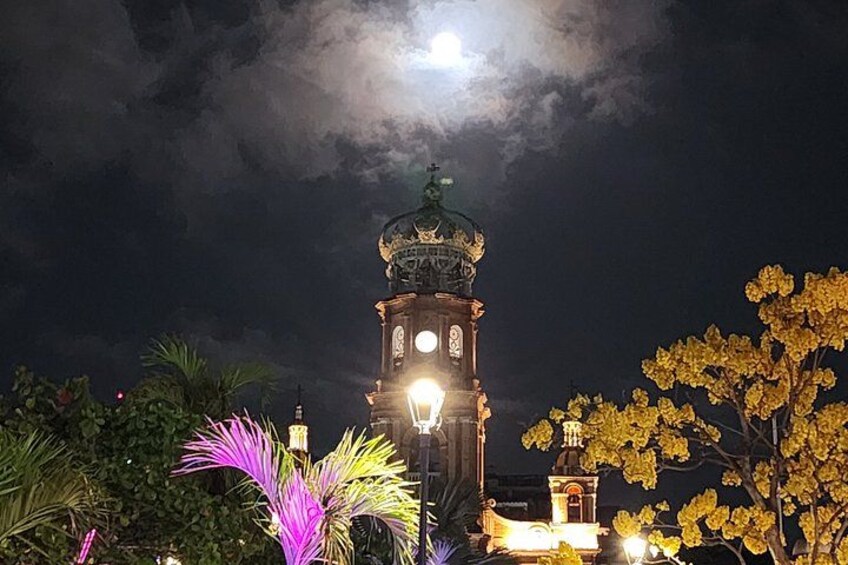 A clock tower illuminated at night with a full moon in the background. 2