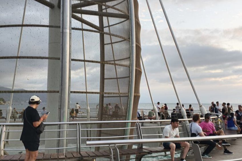 A metal structure with railings, people sitting and standing, and a body of water in the background. 5